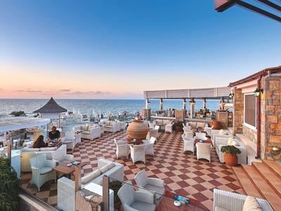 Taras z kafelkową podłogą i miejscami do siedzenia z widokiem na morze o zachodzie słońca.