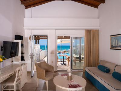 Světý hotelový pokoj s balkonem s výhledem na moře, útulná sedací část a televize.