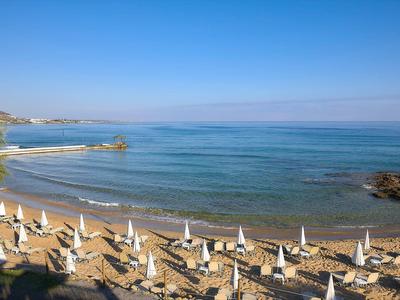 Plaża z rzędami leżaków i parasoli nad spokojnym morzem pod czystym niebem.