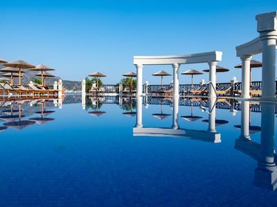 Klidný modrý bazén s slunečníky a sloupy pod jasnou oblohou.