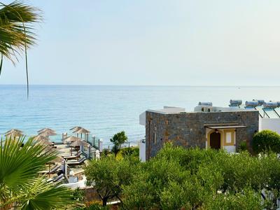 Výhled na moře s hotelovými budovami, palmami a slunečníky za jasného dne.