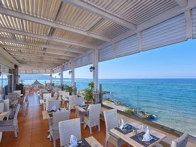 Otevřená restaurace s bílou pergolou a výhledem na modré moře.