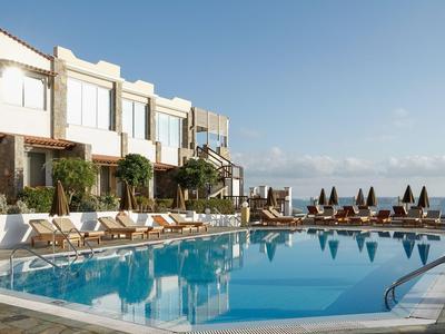 Moderní hotelový bazén s lehátky a výhledem na moře za jasné oblohy.