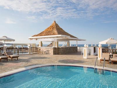 Bazénová oblast s lehátky a slunečníky pod modrou oblohou u moře.