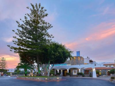 Hotelová budova s velkou palmou a zahradou při západu slunce