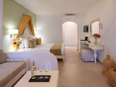 Moderně zařízený hotelový pokoj s manželskou postelí, pohovkou a stolem v teplých barvách.