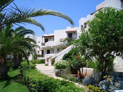 Bílá hotelová budova s palmami a zelenou zahradou pod modrou oblohou.