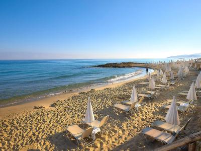 Pláž s pískem, lehátky a zavřenými slunečníky u moře pod jasnou oblohou