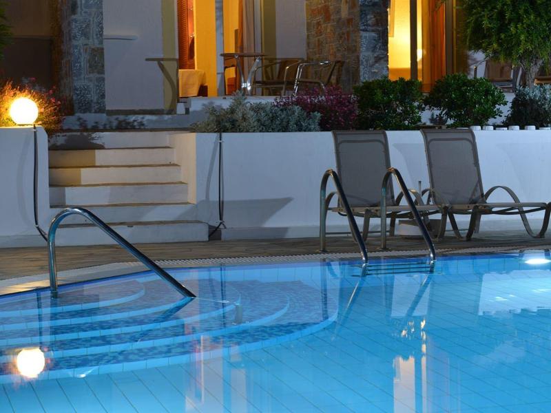 Podświetlany basen przed tarasem z krzesłami w nocy.