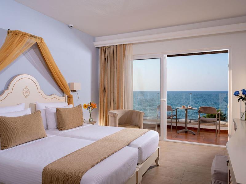 Pokój hotelowy z dwoma pojedynczymi łóżkami, balkonem i widokiem na morze w świetle dziennym.