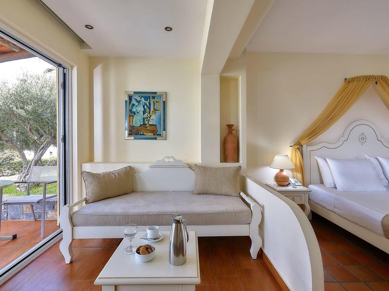 Pokój hotelowy z nowoczesną sofą, łóżkiem, widokiem na taras i ogród.