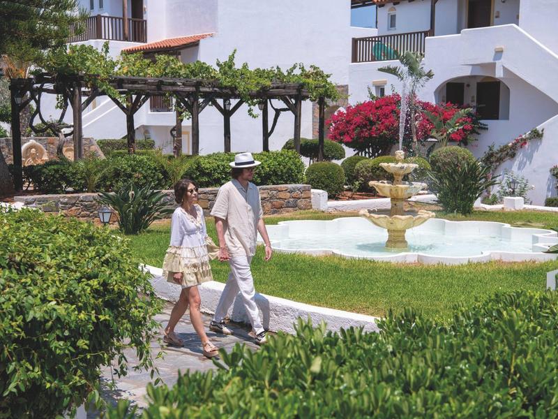 Para spaceruje przez zadbany ogród z fontanną przed budynkiem hotelu.