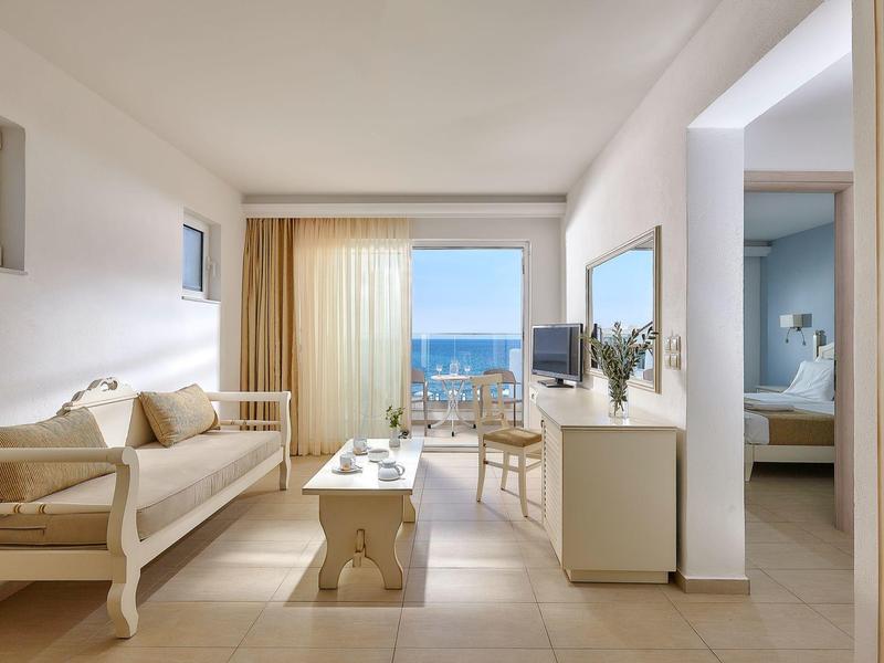 Nowoczesny pokój hotelowy z widokiem na morze, sofą, biurkiem i przyległą sypialnią.