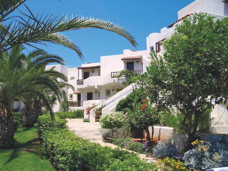 Budynek hotelu z białymi ścianami, otoczony zielonymi palmami i błękitnym niebem.