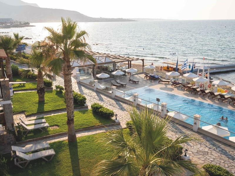 Basen hotelowy z leżakami, palmami i widokiem na morze o zachodzie słońca.