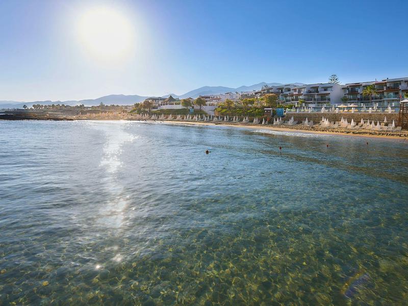 Czyste morze z widokiem na plażę, leżaki i hotele pod jasnym niebem.