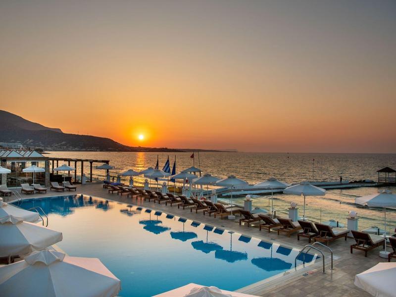 Zachód słońca nad basenem hotelowym z białymi parasolami i widokiem na morze.