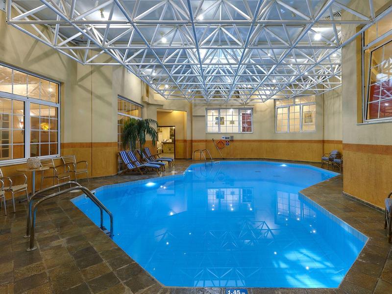 Basen kryty z niebieską wodą, brązową podłogą i białymi belkami sufitowymi w hotelu