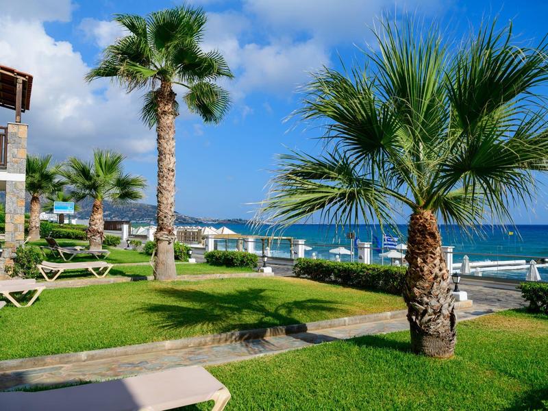 Zielony ogród hotelowy z palmami, leżakami i widokiem na niebieskie morze pod błękitnym niebem.