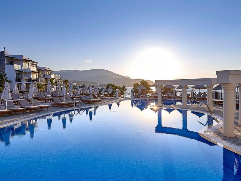 Duży basen na zewnątrz z leżakami i białymi kolumnami o zachodzie słońca