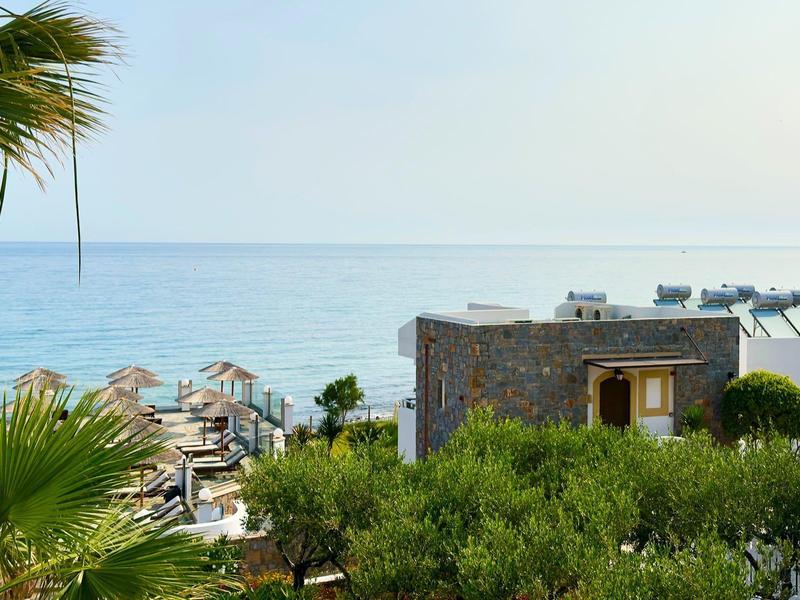 Widok na budynek hotelu z parasolami i morzem w tle w słoneczny dzień.