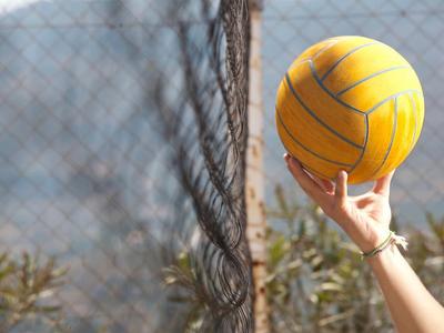 Main tenant un ballon de water-polo jaune devant un filet en plein air