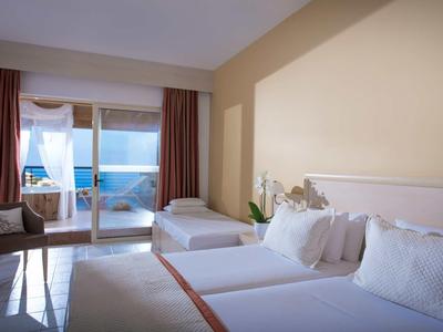 Chambre d'hôtel lumineuse avec deux lits, chaise, balcon et vue sur la mer.