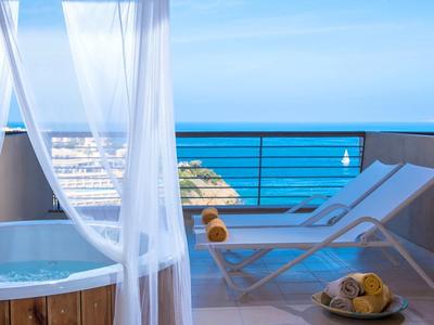 Terrasse avec jacuzzi, chaises longues et vue dégagée sur la mer sous un ciel bleu.
