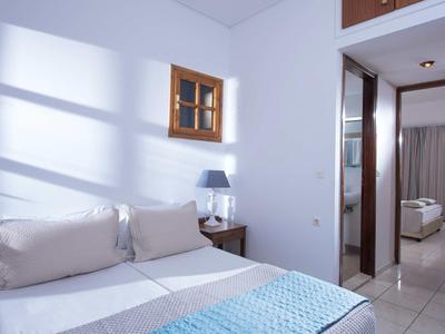 Chambre lumineuse avec literie blanche, fenêtre et salon adjacent.