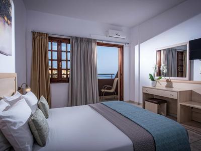 Chambre d'hôtel lumineuse avec lit double, balcon et vue sur la mer au décor sobre.