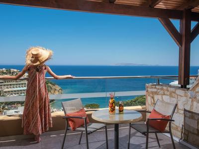Frau mit Hut auf Terrasse schaut auf das Meer mit blauen Stühlen und Tisch.