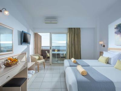 Chambre d'hôtel lumineuse avec deux lits, balcon et vue sur la mer.