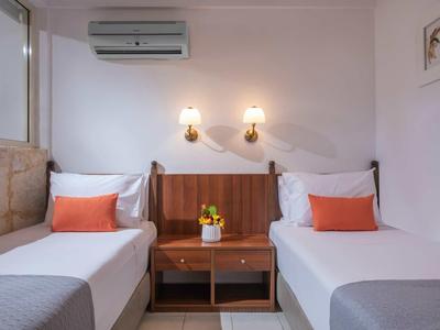 Chambre d'hôtel avec deux lits simples, décoration orange et table de nuit en bois avec fleur.