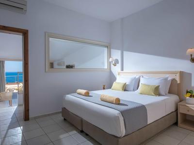 Chambre d'hôtel lumineuse avec lit double, murs blancs et vue sur la mer bleue.