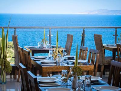 Restaurantterrasse mit Holztischen und Stühlen mit Blick auf das Meer bei klarem Himmel.
