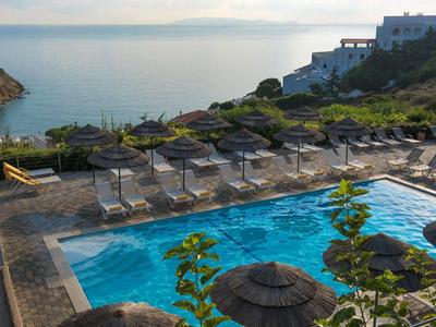 Piscine avec parasols surplombant la mer et des bâtiments proches au coucher du soleil.