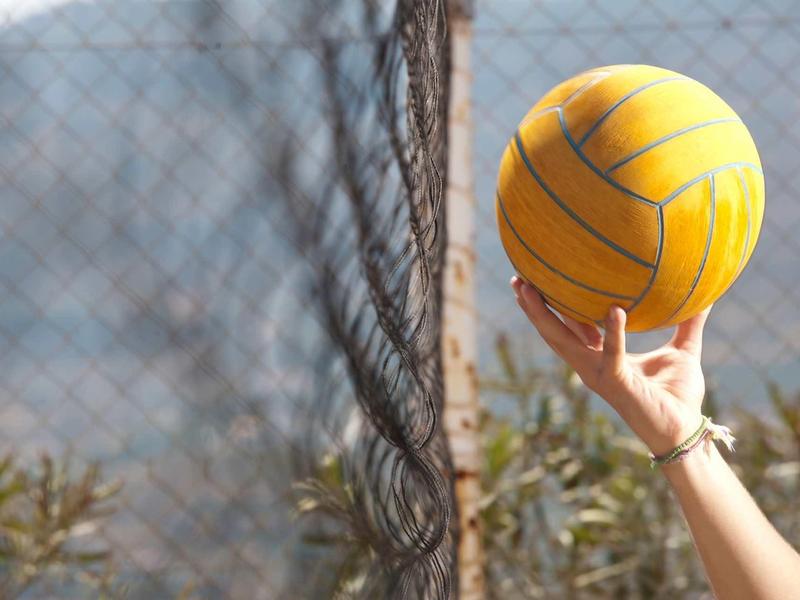 Main tenant un ballon de water-polo jaune devant un filet en plein air