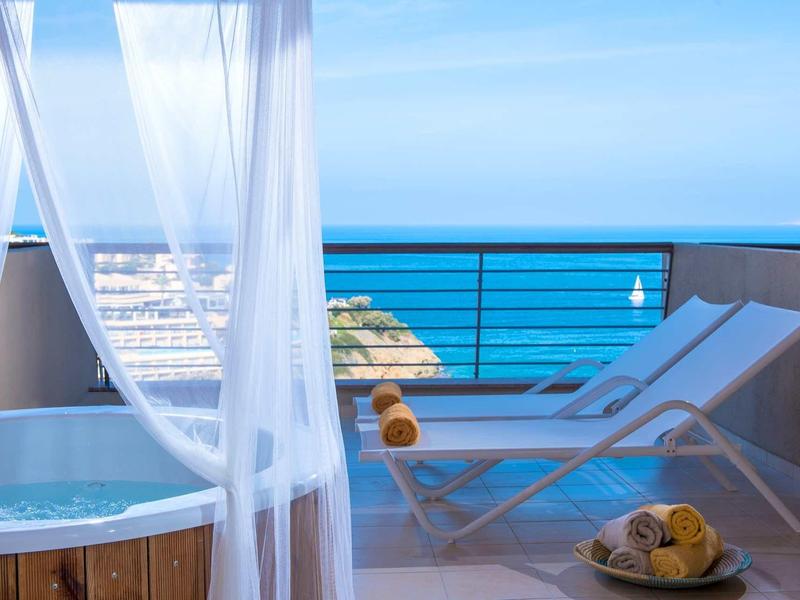 Terrasse avec jacuzzi, chaises longues et vue dégagée sur la mer sous un ciel bleu.