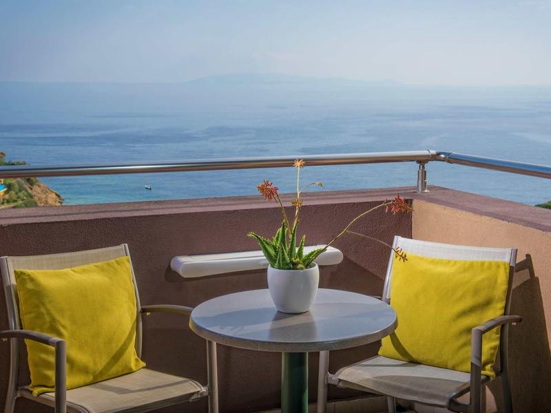 Balcon avec deux chaises et table donnant sur la mer et un ciel bleu.
