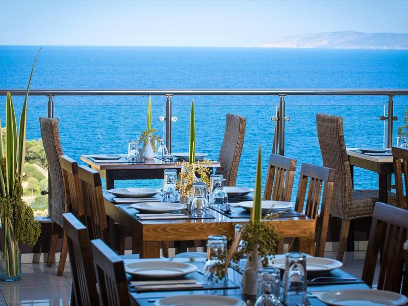 Terrasse de restaurant avec tables en bois dressées et vue sur la mer bleue.