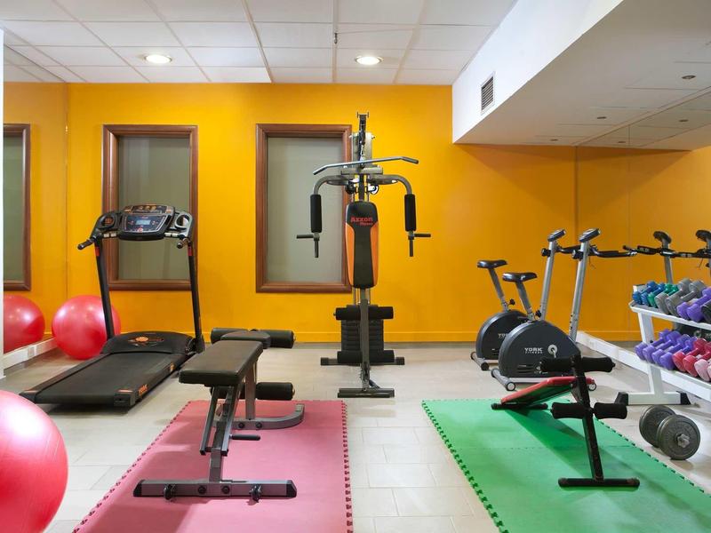 Salle de sport moderne d'hôtel avec murs jaunes, machines d'entraînement et tapis colorés.