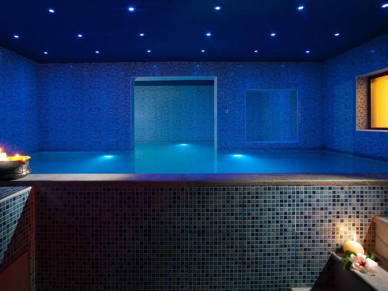 Espace spa relaxant avec piscine éclairée en bleu et lumière de bougie.