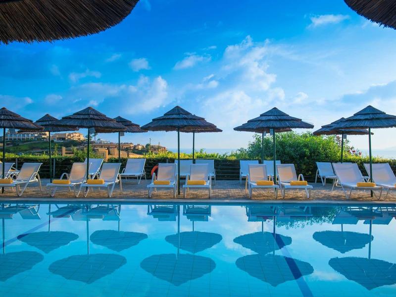 Piscine avec transats et parasols sous un ciel bleu au bord de la mer.