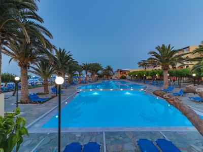 Zona piscina dell'hotel illuminata con palme e sdraio al crepuscolo.