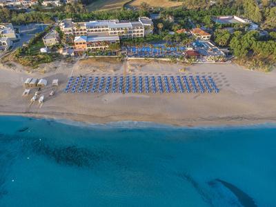 Letecký pohled na resort s písečnou pláží, modrými slunečníky a tyrkysovým mořem.