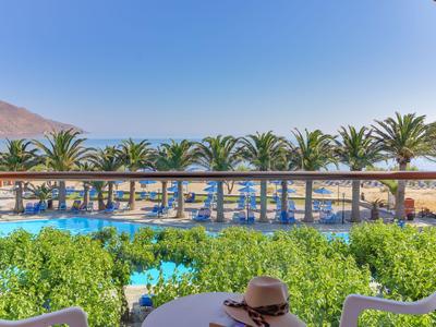 Vista di una piscina dell'hotel con palme e spiaggia sullo sfondo sotto un cielo limpido.
