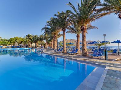 Piscina con palme e ombrelloni vicino al mare sotto un cielo limpido