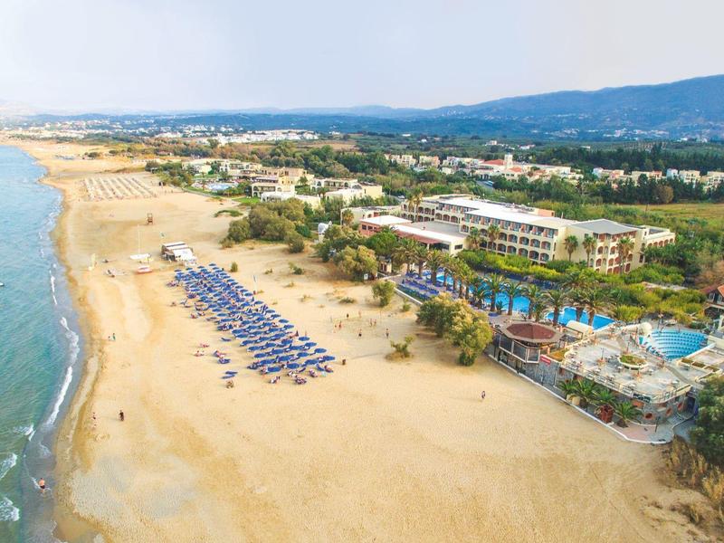 Dlouhá písečná pláž s deštníky vedle resortu s bazénem a zelenými stromy