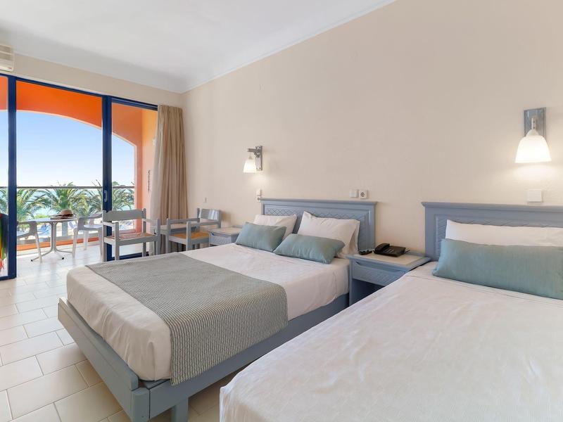 Hotelový pokoj se dvěma postelemi, moderním nábytkem a balkonem s výhledem na moře.