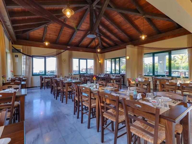 Světlá restaurace s dřevěným nábytkem, prostřenými stoly a velkými okny s výhledem na zeleň.